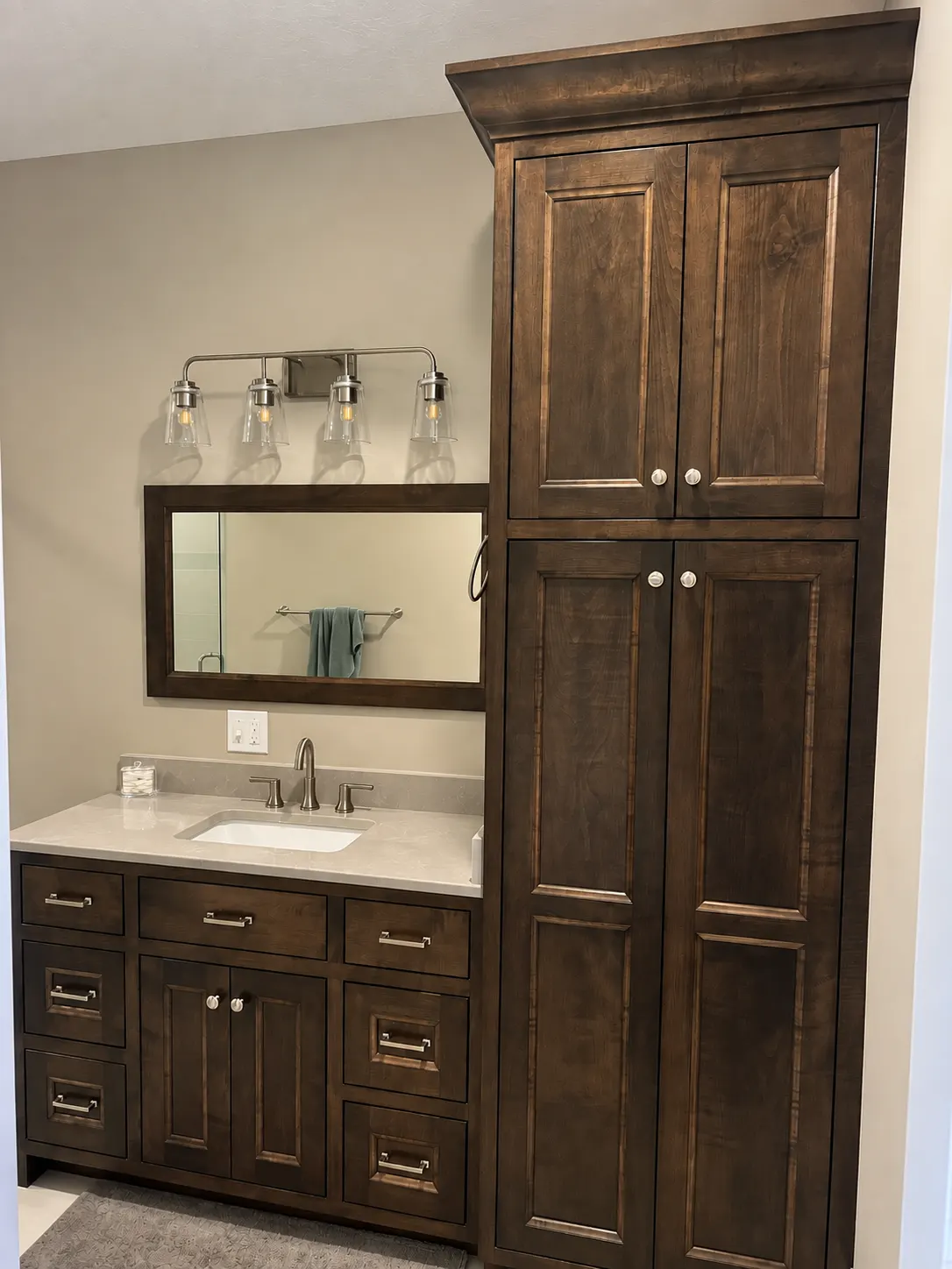 Stained bathroom vanity beside a tall linen cabinet